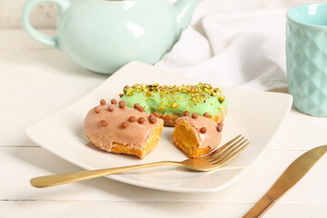 Plate with sweet eclairs and tea on light background