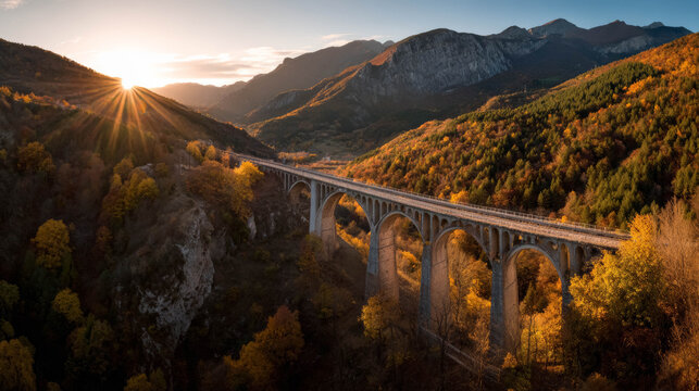Autumn scenery featuring a railway bridge crossing a valley, surrounded by colorful foliage and majestic mountains, illuminated by sunset glow - Powered by Adobe