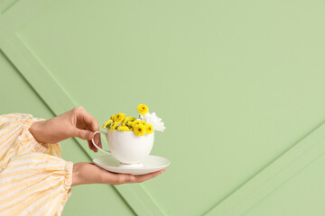 Female hands holding cup with beautiful flowers on green background