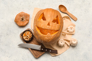 Carved Halloween pumpkin with bowl of seeds, candles and knife on white grunge background