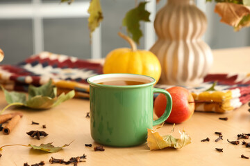 Autumn leaves, cup of hot green tea, apple and scattered spices on table in kitchen