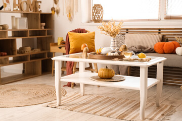 Coffee table with teapot, cup of green tea and autumn decor in interior of living room