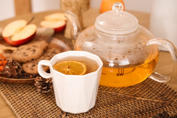 Teapot, cup of green tea, plate with cookies and autumn decor on table in room. Closeup