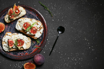Plate of delicious fig bruschetta with ricotta cheese and arugula on black background