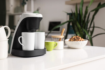 Coffee machine with cups on table in office, closeup