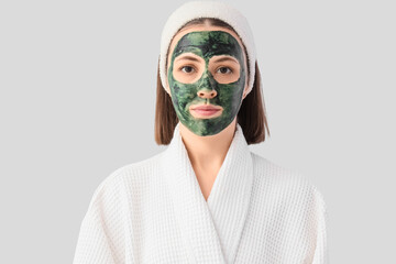Young woman with spirulina facial mask on light background