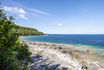 Picturesque shoreline of Flowerpot Island in Ontario, with vibrant blue waters and lush greenery under a clear sky.