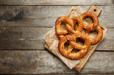 Cutting board with tasty pretzels on grey wooden background, closeup