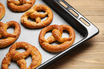 Baking tray with tasty pretzels on wooden background, closeup
