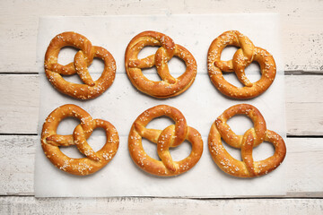 Parchment paper with tasty pretzels on white wooden background, closeup