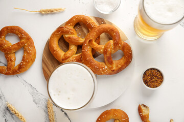 Board with glasses of beer and pretzels on marble background, closeup