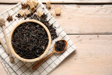 Bowl and spoon with dry black tea leaves on white wooden background