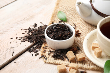 Bowl with dry black tea leaves and cubes of sugar on white wooden background, closeup