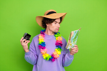 Cheerful young man wearing colorful lei and hat, holding camera and map, standing against vibrant...