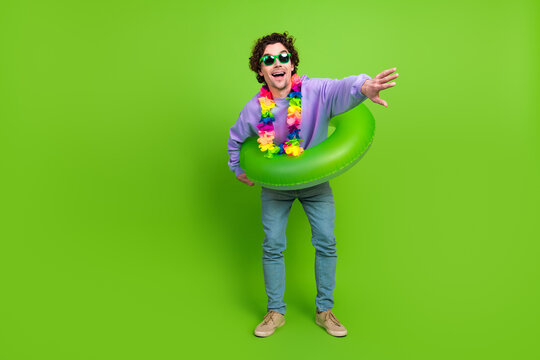 Cheerful young man in casual outfit with a colorful lei and inflatable ring posing playfully against a green background - Powered by Adobe