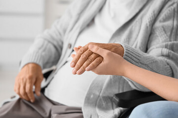 Senior woman in wheelchair with granddaughter holding hands at hospital, closeup