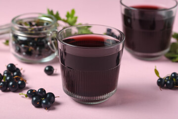 Glasses of fresh black currant juice and jar with berries on pink background, closeup