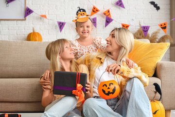 Cute girls with gift and their grandmother celebrating Halloween at home