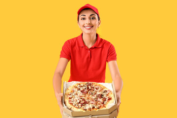 Female courier with tasty pizza on yellow background