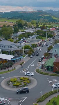 Aerial view of a roundabout in Matakana in New Zealand. Cars are driving and parked along the street. A worker in orange is directing traffic.