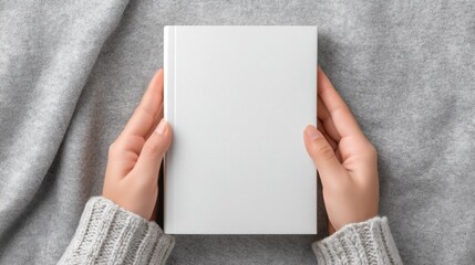 Hands Holding a Blank White Book on a Soft Grey Fabric Background, Cozy Winter Scene with a Comfortable Vibe for Creative Projects and Content