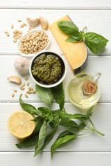 Fresh pesto sauce in bowl and ingredients on white wooden table, flat lay