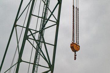 Green crane with large hook on yellow block hung by chains