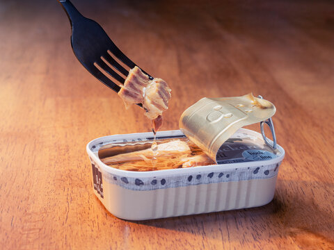 An open can of canned mackerel in oil with a fork pulling fish out of the can