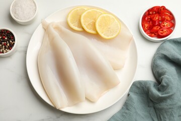 Pieces of raw squids with lemon and spices on white marble table, flat lay