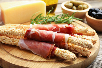 Delicious grissini sticks with sesame seeds and prosciutto on wooden table, closeup