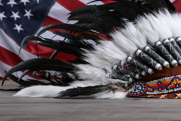 Native American chief headdress (feathered war bonnet) on wooden surface against American flag,...