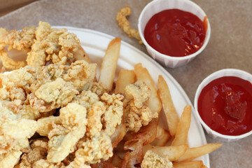 golden fried clams with fries on paper plate with two cups of ketchup