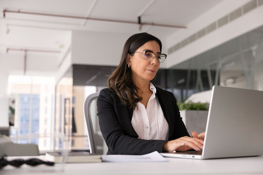 Serious mature business leader woman in glasses typing on laptop