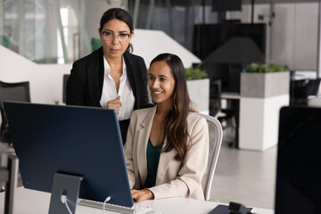 Senior businesswoman standing by happy young professional working at computer