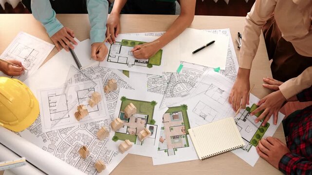 Architect and safety engineer discussion about building construction use blueprint on table with architectural document, measurement tool and wooden block scatter around at modern office. Delineation.