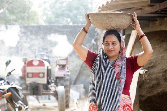 Indian rural working in village while carrying cow dung, cake, poor, recycle, at village. Rural women carrying cow dung cakes on the head used as cooking fuel in village.