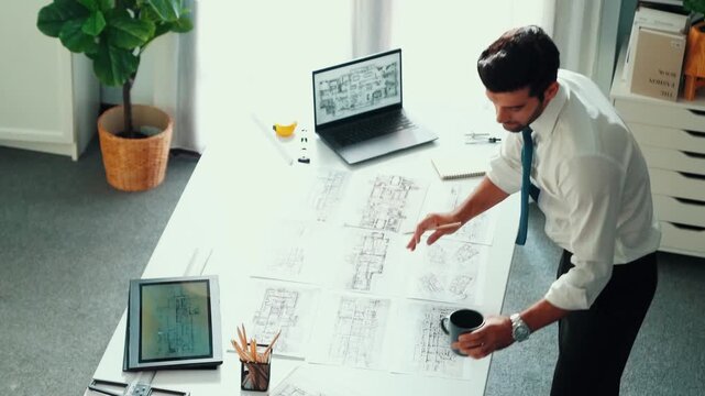 Architect engineer using laptop planning house design at office while sitting at meeting table with blueprint and equipment scatter around.Skilled civil engineer working at blueprint. Alimentation.