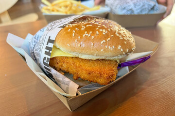 Crispy chicken sandwich with cheese and lettuce in a cardboard box.