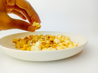Hand picking up sweet caramel Popcorn on a round plate, isolated on a white background.