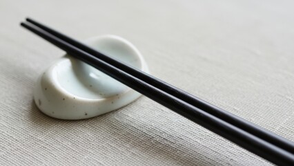 A pair of black chopsticks resting on a ceramic chopstick holder.