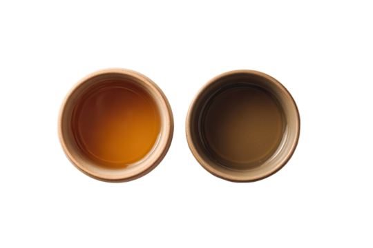 Two small, light brown ceramic cups, one with amber liquid, the other with darker liquid, top view