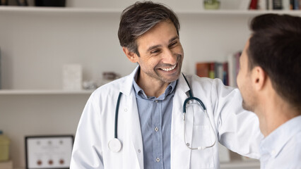 Compassionate doctor place hand on patient shoulder with kind smile