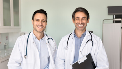 Two smiling doctors standing in clinic office looking at camera