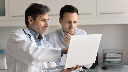 Obraz premium Confident male doctor consulting patient in clinic office using notebook