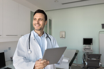 Smiling male doctor standing in ultrasound diagnostics office holding pad
