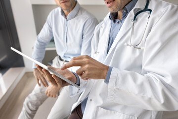 Closeup tech-savvy male doctor using tablet on meeting with patient