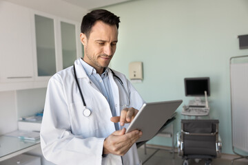 Busy male doctor using tablet in office with ultrasound equipment