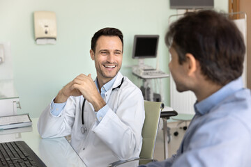 Fototapeta premium Friendly middle aged doctor hold casual conversation with male patient