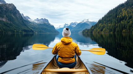 Traveler yellow jacket paddles canoe serene mountain lake, surrounded by majestic peaks and lush