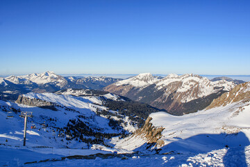 Scenic view of the French Alps with snowy peaks and a chairlift under clear blue sky. Winter...